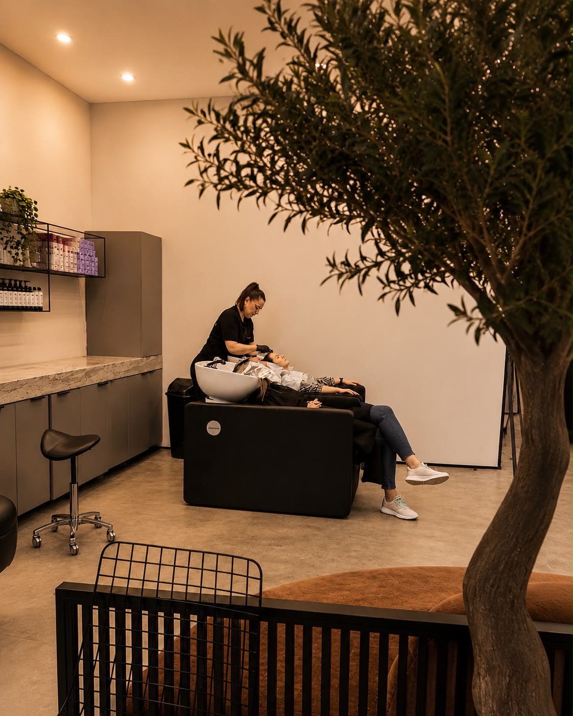 Stilistă Headen la spălat, având grijă de o clientă, lângă măslinul din salon